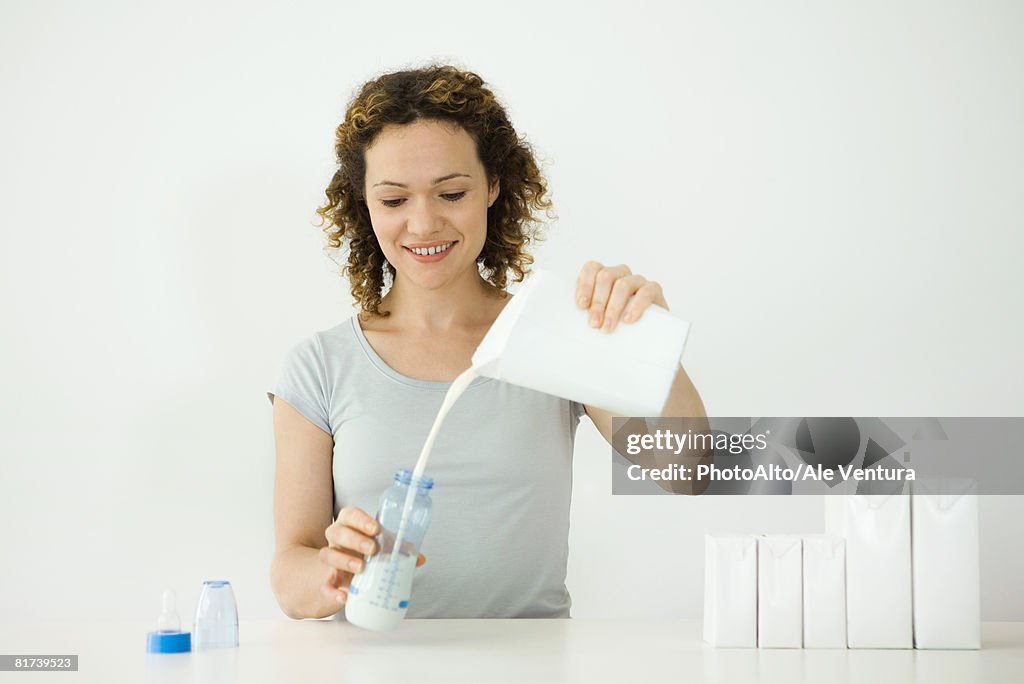 Woman pouring milk from carton into baby bottle, smiling