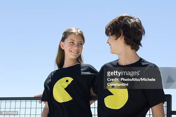 young couple wearing tee-shirts printed with graphic characters, smiling at each other - casal adolescente imagens e fotografias de stock