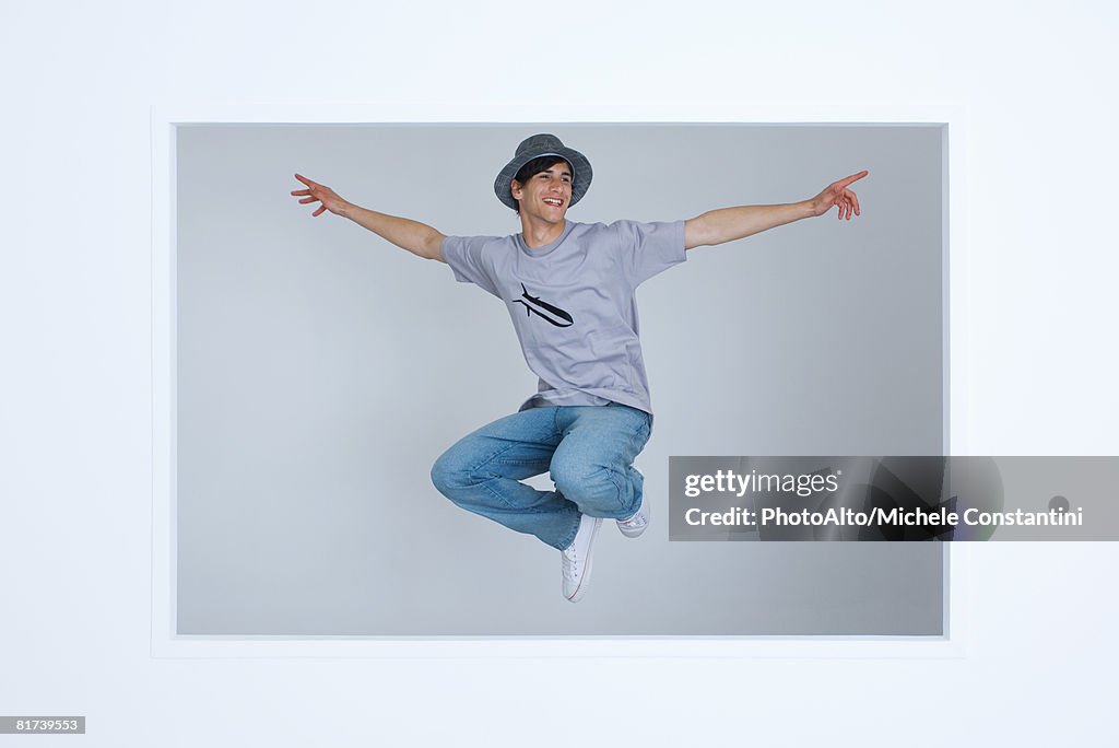 Young man wearing tee-shirt with bomb graphic, jumping in midair, arms outstretched