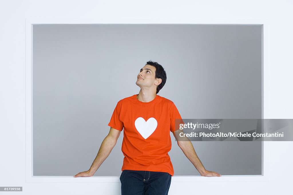 Man wearing tee-shirt with heart symbol, looking up, smiling