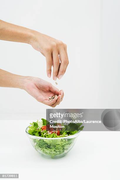 woman sprinkling sunflower seeds on salad, cropped view of hands - sprinkling imagens e fotografias de stock