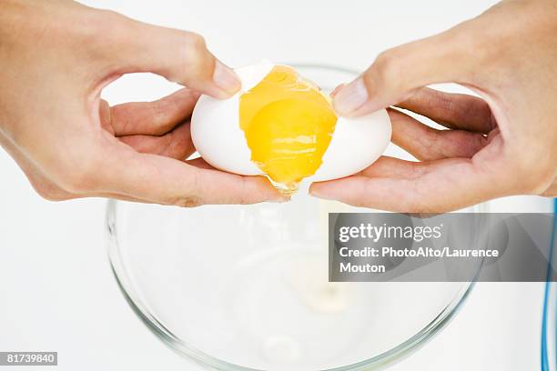 woman cracking egg into mixing bowl, cropped view of hands, high angle view - cracked egg stock-fotos und bilder