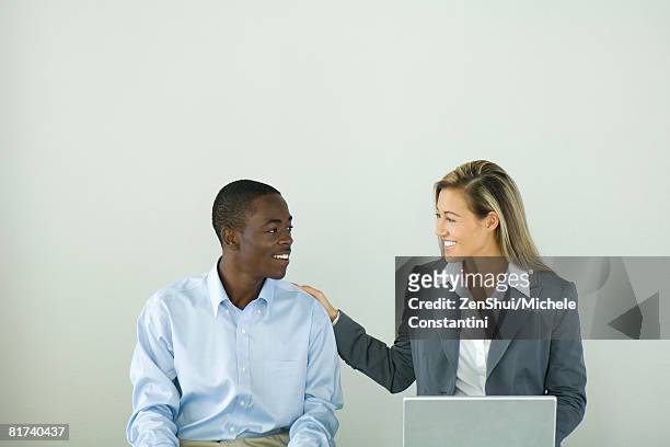 businesswoman sitting next to teenage boy with her hand on his shoulder, both smiling at each other - laptop coloured background stock pictures, royalty-free photos & images