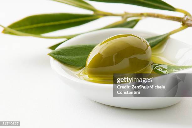 green olive and sprig of leaves in small dish of olive oil, close-up - olive oil ストックフォトと画像