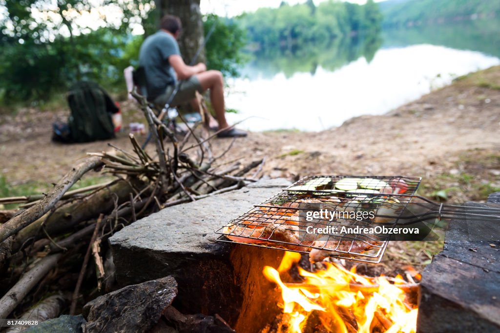 Fisherman preparing dinner on campfire, adventure lifestyle camping fishing concept