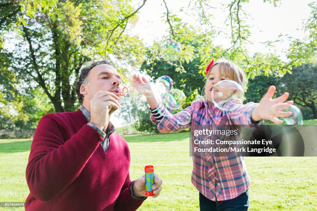 Father and daughter blowing bubbles in garden