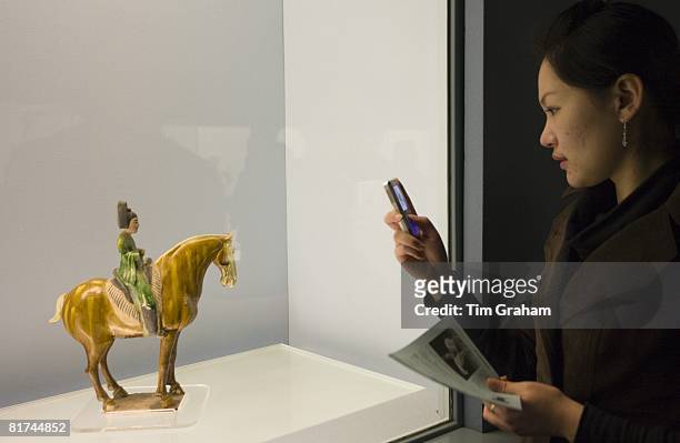 Woman takes a photograph using a mobile phone of an object on display in the Shanghai Museum, China