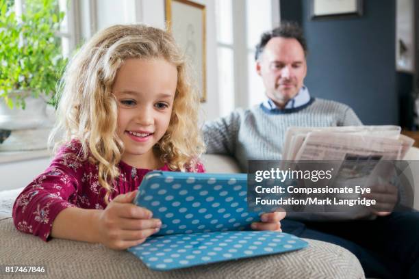 father reading newspaper and daughter using digital tablet in living room - speckled sussex stock pictures, royalty-free photos & images