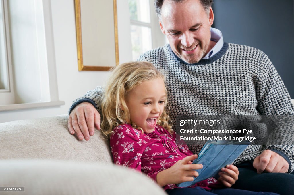 Father and daughter using digital tablet on sofa in living room