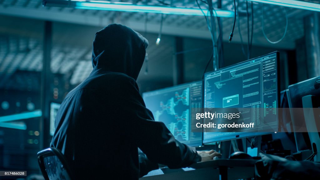 Tiro de la parte posterior de Hacker encapuchado en servidores de datos corporativos desde su escondite subterráneo. Lugar tiene atmósfera oscura, varias pantallas, Cables por todas partes.