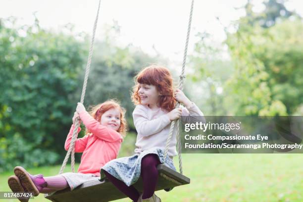 twin girls swinging in backyard - lewes england stock-fotos und bilder