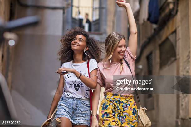 twee jonge vrouwen vrienden plezier delen van muziek in de straat - gedeelde mobiliteit stockfoto's en -beelden