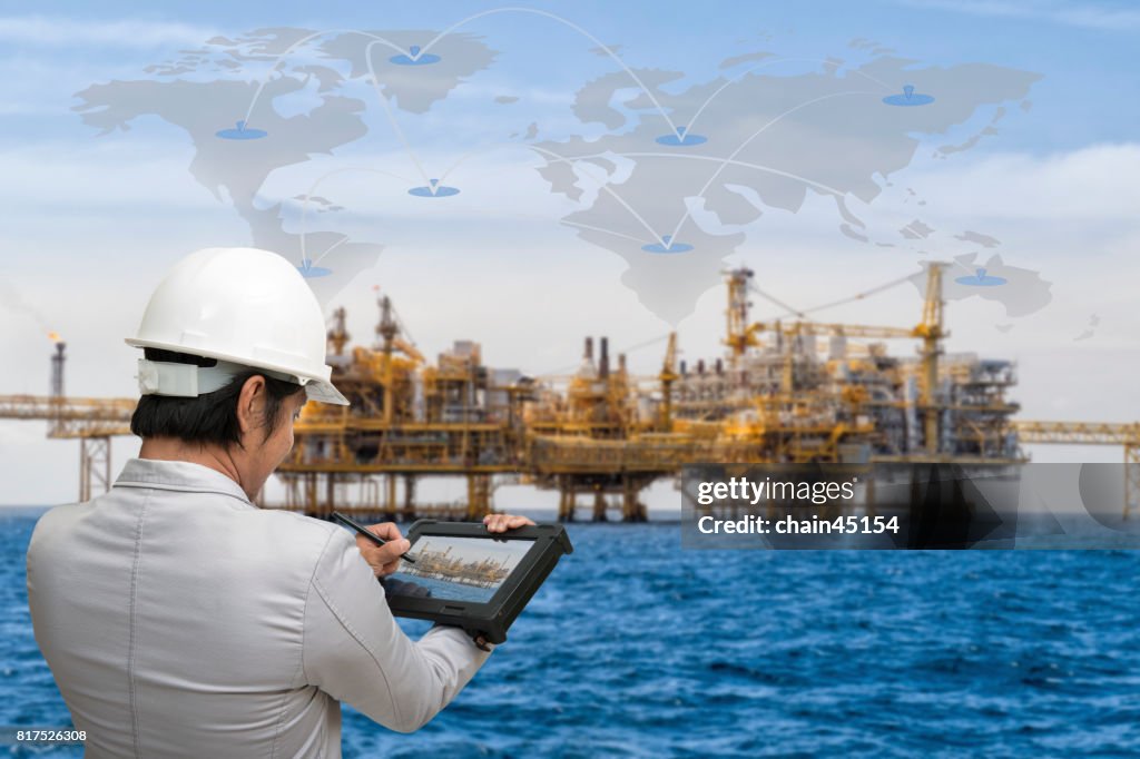 Engineer working with tablet PC near Oil and gas jack up drilling rig in the ocean sea from oil and gas industrial petroleum.