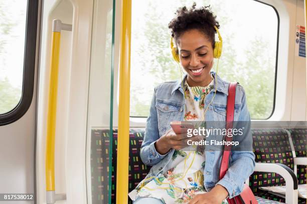 woman using her phone on a train - listening stock-fotos und bilder