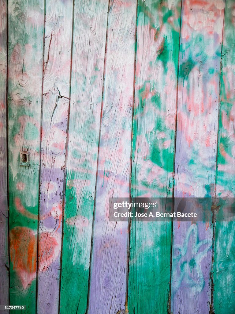 Full Frame  textures of from a wooden door abandoned painted in various colors by graffiti and closed with a chain