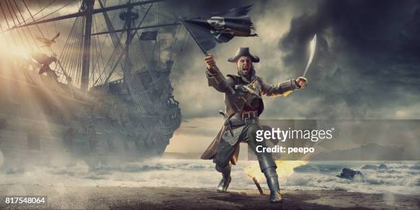 piraat op strand holding vlag en cutlass in de buurt van piratenschip - schooner stockfoto's en -beelden
