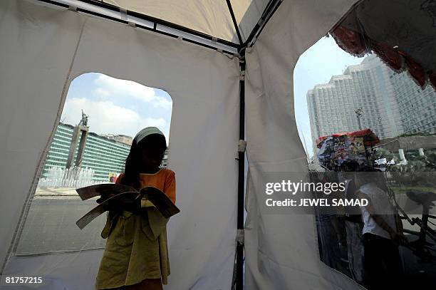 Girl reads a book inside a makeshift public library set up on a main street during the "Car Free Day" in downtown Jakarta on June 29, 2008. Usually...