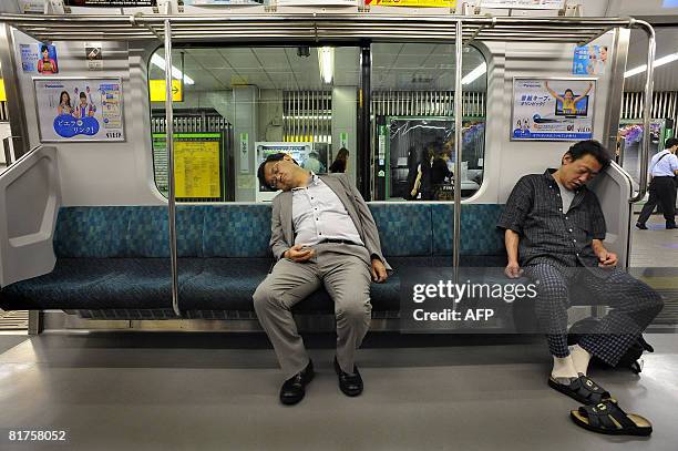 Two passengers sleep as they travel on the Japan Railways above-ground commuter line of the subway train system of Tokyo on June 17, 2008. Though not...