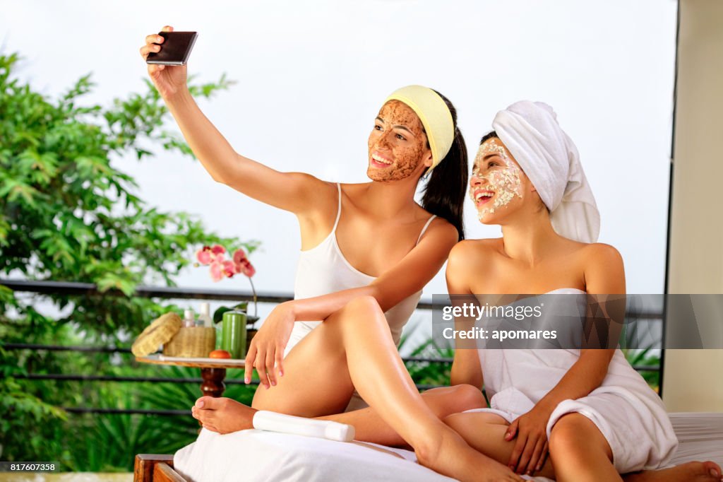 兩個西班牙裔美國人的年輕女人做美容護理在家或水療時採取自拍照。