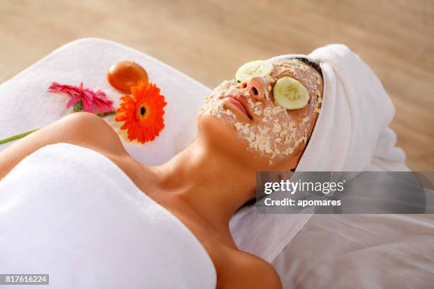 mulher jovem hispânica deitado na cama e ficando aveia rosto esfoliante e descansando com fatias de pepino sobre os olhos. - oatmeal - fotografias e filmes do acervo