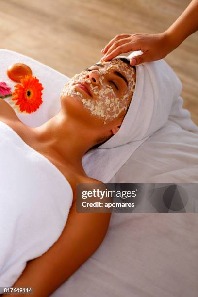 hispanic young woman laying on bed and getting oatmeal face scrub after bath. skin exfoliation. - oatmeal stock pictures, royalty-free photos & images