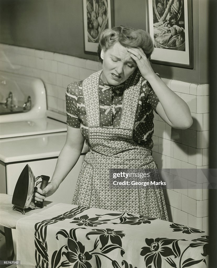 Mature woman ironing with hand to head