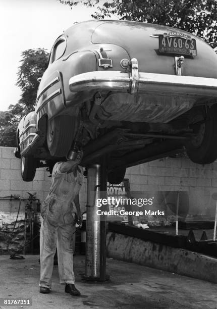 mechanic working on underside of car - hebebühne stock-fotos und bilder