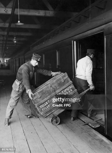 Two men, one of whom is armed, load Wells Fargo express packages onto a train, USA, circa 1925.