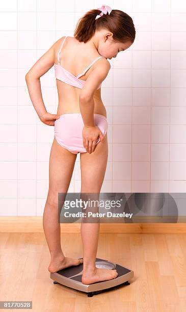 girl concerned with body shape on bathroom scales. - weight gain foto e immagini stock