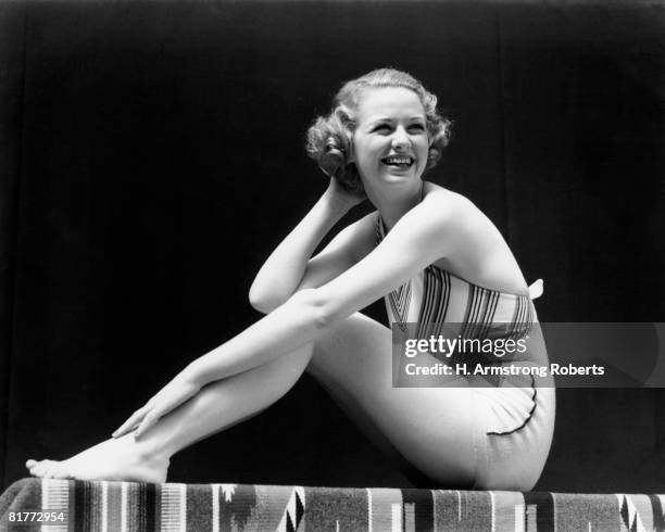 smiling blonde woman wearing 2 piece bathing suit striped halter top sitting full figure profile posing pose bench indian blanket retro. - 1930 stock pictures, royalty-free photos & images