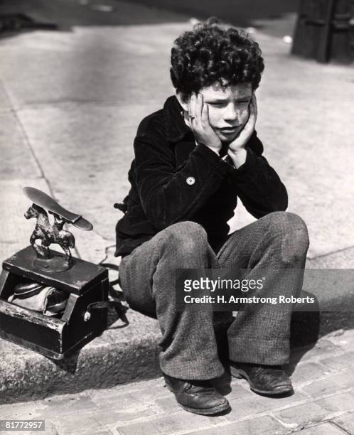 sad boy, curly hair sitting on curb patched trousers shoeshine kit work working worker shoe shine poor poverty depression rrr retro. - 1930 photos et images de collection