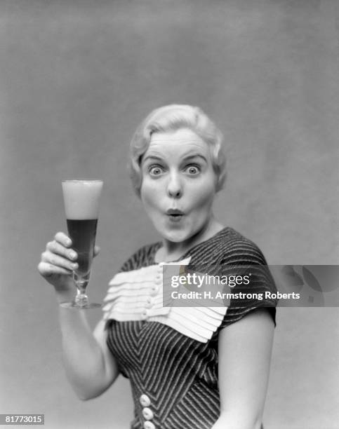 blonde woman in black dress with stripes & white buttons & trim holding a pilsner glass of beer with a large head with pursed lips & poppy eyes cartoon. - 1930 stock pictures, royalty-free photos & images