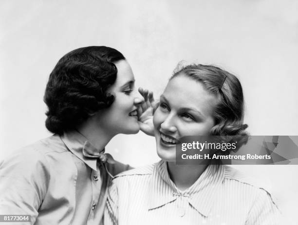 two smiling women the 1 wearing the blouse with a bowtie is wispering a secret in the ear of the i wearing a shirt & collar pin blonde teeth. - 1930s woman stock pictures, royalty-free photos & images