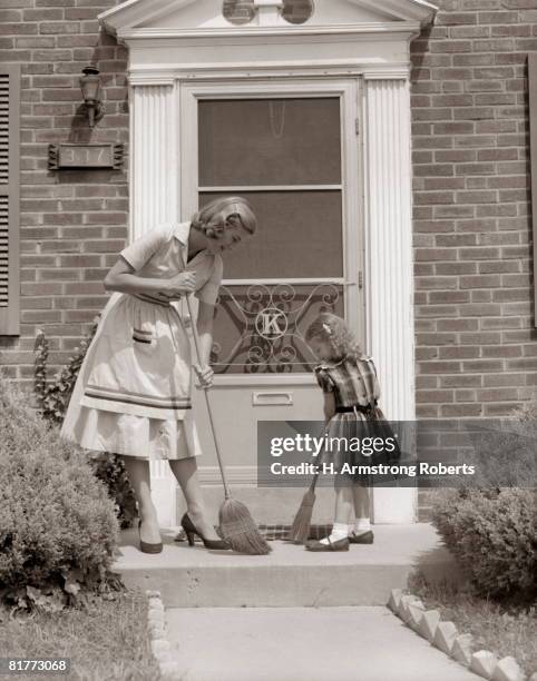 mother and daughter sweeping steps at front door of house. - 1950s housewife stock-fotos und bilder