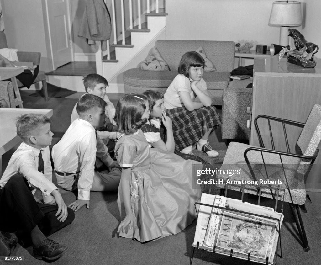 Side View Of 3 Pairs Of Girls & Boys Dressed Up Gathered Around Television Set.
