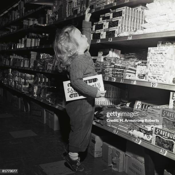 toddler in candy aisle of store supermarket grocery standing on toes reaching for box of candy on shelf hold box lollipops shopping retro cute. - girl toes stock pictures, royalty-free photos & images