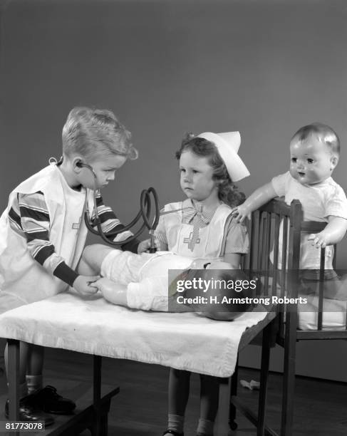 boy & girl playing doctor & nurse using doll as a patient the boy is wearing a doctor's outfit using a toy stethoscope the girl is dressed as nurse. - vestita da dottoressa foto e immagini stock