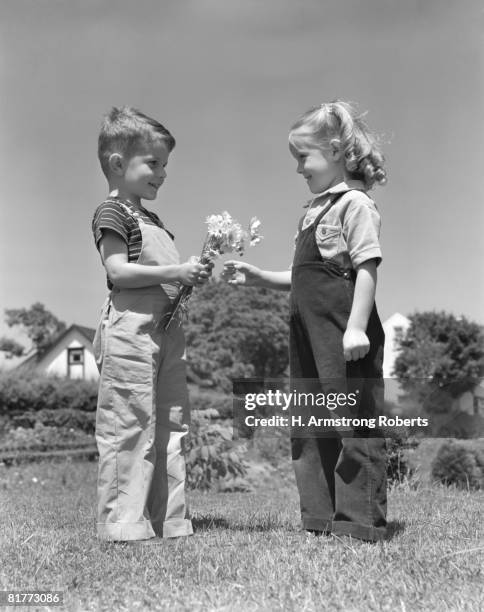 couple boy giving bouquet flowers daisies to little girl spring summer romance flirt both wear bib overall type outfits. - bib overalls stockfoto's en -beelden