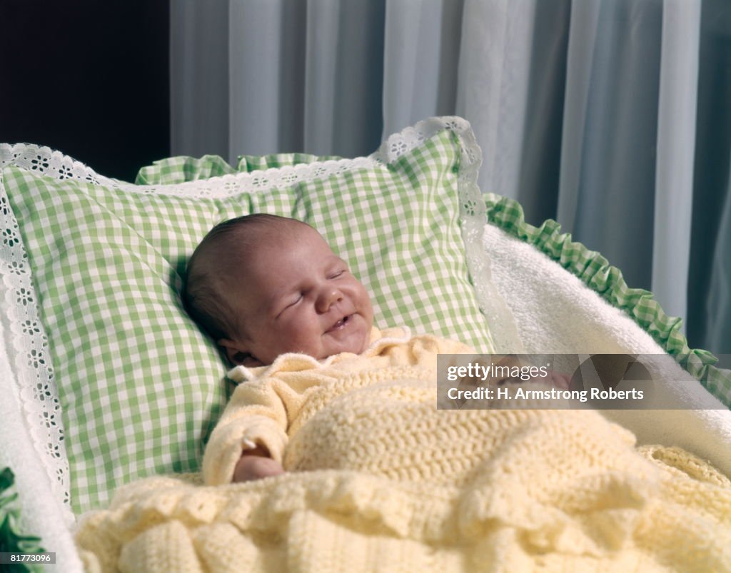 Sleeping Baby In Bassinet With Yellow Blanket Green And White Pillow.