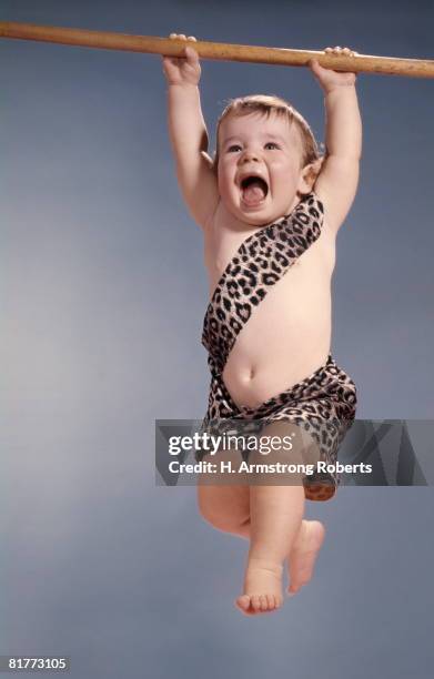 baby in tarzan leopard skin costume hanging swinging from tree limb yelling. - dierenprint stockfoto's en -beelden