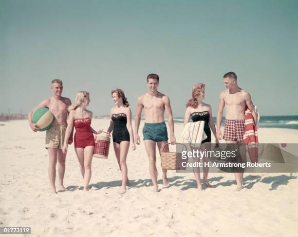 3 teen couples 6 people walking in a line down beach summer carry basket thermos beach ball towels umbrella. - fünfziger jahre stock-fotos und bilder