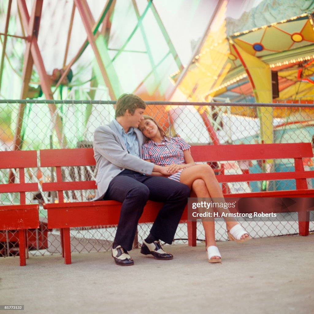 Couple Sitting On Bench At An Amusement Park.