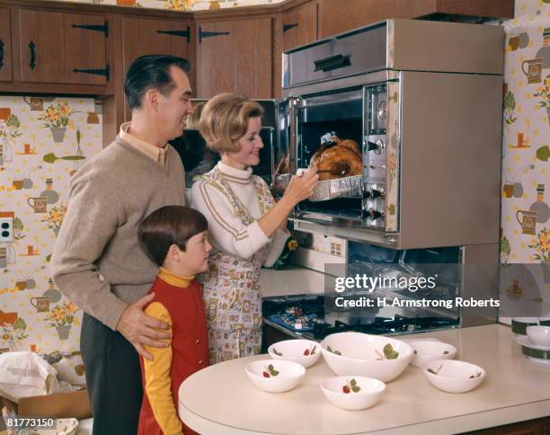 woman taking roast turkey out of wall oven with husband and daughter watching family man girl food holiday. - american diner stockfoto's en -beelden