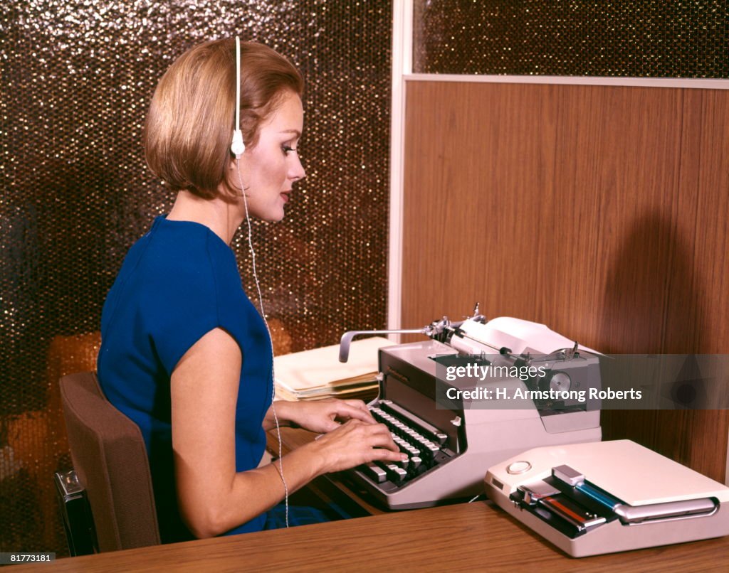 Woman Secretary Typing Typewriter Listening To Dictation On Tape Recorder Earphones Headset Desk.