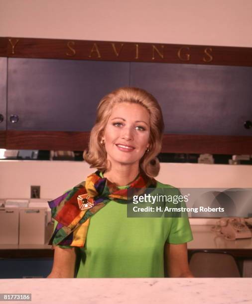 smiling blond blond woman green dress with scarf bank teller cashier. - 1960 fotografías e imágenes de stock