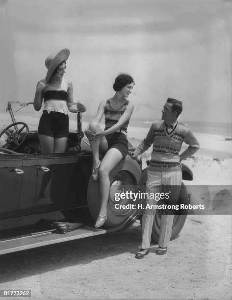 2 women bathing suits posed on convertible car with man in striped trousers and vest looking on upscale fashion wealth leisure straw hat. - women in the 1920's stockfoto's en -beelden