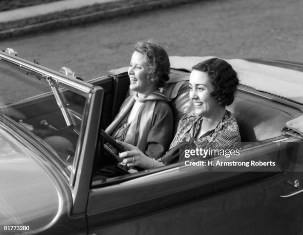 women both are laughing while the driver's wearing a wedding band & lace shawl driving a convertible coupe with the top down carefree fun. - car top down stock pictures, royalty-free photos & images