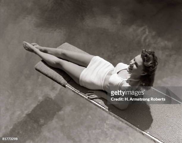 woman lying on diving board over pool sunbathing two piece bathing suit summer. - badeanzug stock-fotos und bilder