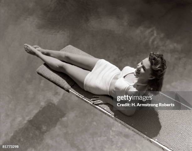 woman lying on diving board over pool sunbathing two piece bathing suit summer. - 1940 fotografías e imágenes de stock