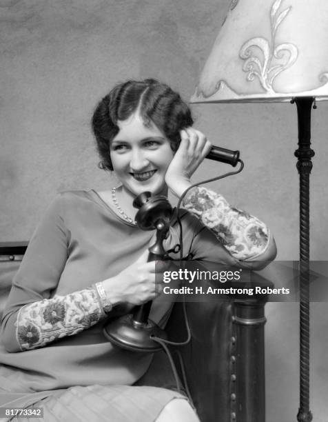 woman on candle stick phone sitting on couch by lamp smiling flirting. - antique phone stock pictures, royalty-free photos & images